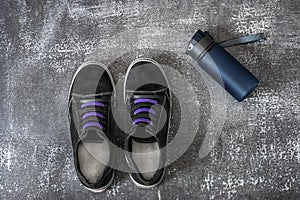 Black sports sneakers with two-tone laces along with a blue plastic container with water on a gray surface