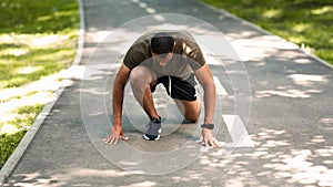 Black sportsman in starting position, ready to run at park on sunny day