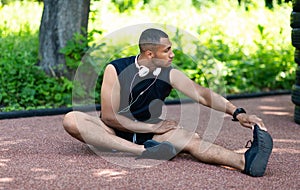 Black sportsman stretching on road at park after his morning run