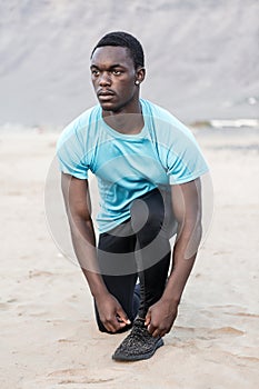 Black sportsman tying shoelaces on beach