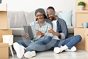 Black Spouses With Digital Tablet Sitting Among Cardboard Boxes In New Flat