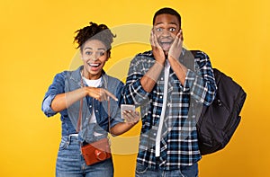 Black Spouses Pointing Finger At Phone Recommending Application, Yellow Background