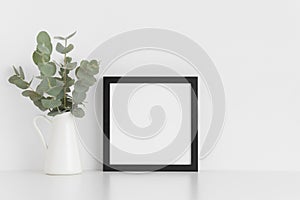 Black square frame mockup with a bouquet of eucalyptus in a vase on a white table.Portrait orientation
