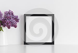 Black square frame mockup with a bouquet of lilac in a vase on a white table