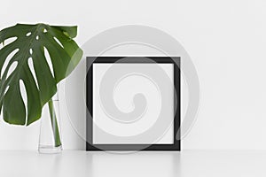 Black square frame mockup with a monstera leaf in a glass vase on a white table