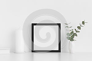 Black square frame mockup with workspace accessories and eucalyptus in a vase on a white table