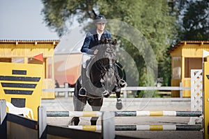 Black stallion horse and handsome man rider jumping obstacle