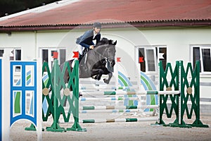 Black stallion horse and handsome man rider jumping obstacle