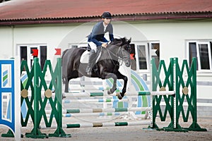 Black stallion horse and handsome man rider jumping obstacle during showjumping competition