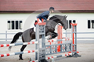 Black stallion horse and handsome man rider jumping obstacle during showjumping competition