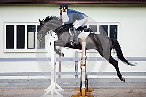 Black stallion horse and handsome man rider jumping obstacle during showjumping competition photo