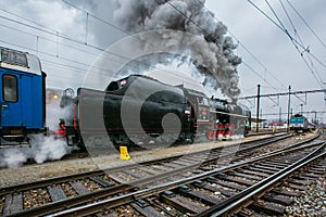 Black steam engine with tender and red wheels belching out steam