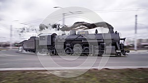 Black steam locomotive drifts on the road in the city