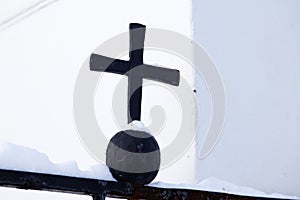 Black steel cross on gate to church in winter