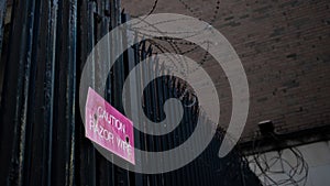 Black steel fence with razor wire and red caution warning sign