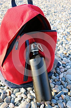 Black  steel water bottle in front of red travel backpack.  Eco package concept