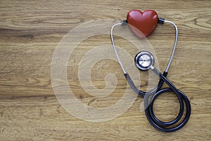 Black stethoscope with red heart of doctor for checkup on wood table background.