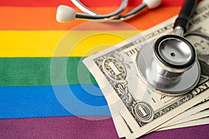 Black stethoscope and US dollar banknotes money on rainbow flag background, symbol of LGBT pride month  celebrate annual in June