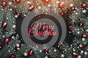 Black stone background with a frame of fir branches decorated with balls and red ribbon