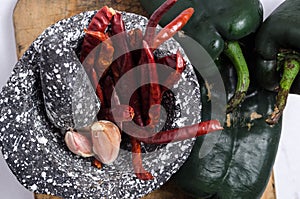 Black stone mortar with ingredients for sauce, red chili peppers, raw garlic cloves
