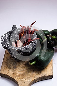 Black stone mortar with ingredients for sauce, red chili peppers, raw garlic cloves.