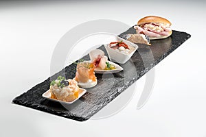 Black stone rectangular tray with shrimp tartare snack cannoli swordfish ravioli with robbiola tartina nordica mousse aubergine photo