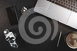 Black stone table with retro photo camera, laptop or notebook computer, phone and coffee