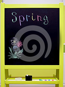 Black student chalk board with a stand for chalk and multi-colored inscription spring