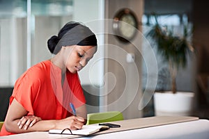 Black student making notes in her notebook sitting at home