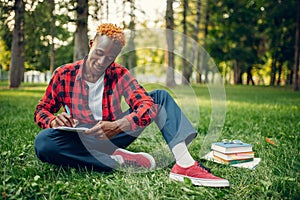 Black student writing in notebook on the grass