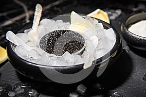 Black Sturgeon caviar on ice with pearl spoon, sour cream, lemon on slate plate and dark marble background