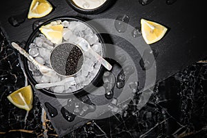 Black Sturgeon caviar on ice with pearl spoon, sour cream, lemon on slate plate and dark marble background