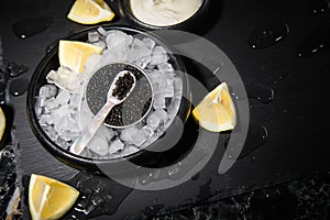 Black Sturgeon caviar on ice with pearl spoon, sour cream, lemon on slate plate and dark marble background