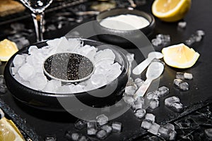 Black Sturgeon caviar on ice with pearl spoon, sour cream, toast, lemon and vodka in lead glass on slate plate and dark marble