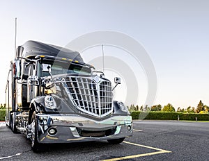 Black stylish big rig semi truck with bright chrome grille stand on wide parking lot