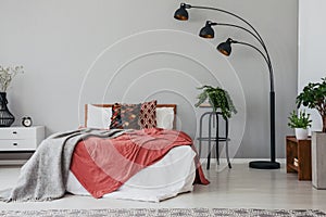 Black stylish lamp in elegant bedroom interior with comfortable double bed, plants, and bedside table