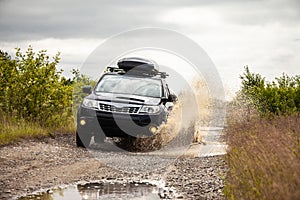 Black Subaru Forester driving on a  dirt road with puddles