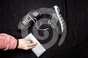 Black suede sneakers decorated with silver sequins and a female hand with a silver purse on a black woven background