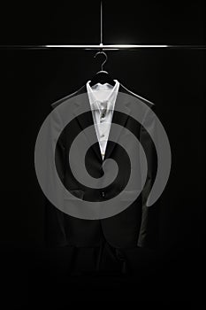 Black suit with a white shirt displayed on a hanger against a dark background