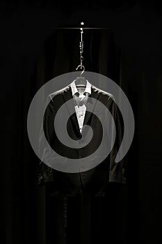 Black suit with a white shirt displayed on a hanger against a dark background