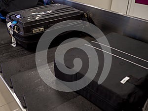 Black suitcases on luggage conveyor belt in the baggage claim at airport, summer travel concept