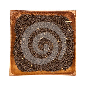 Black sunflower seeds in a wooden bowl on a white background