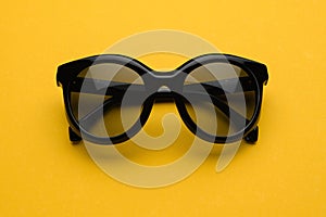 Black sunglass with round frame. Fashion sunglasses front view on summer yellow background. Woman stylish eyeglasses for
