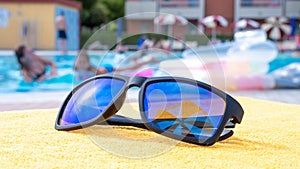 Black sunglasses summer background. Beach pool equipment with travel sunglasses on yellow holiday towel. Sun glasses
