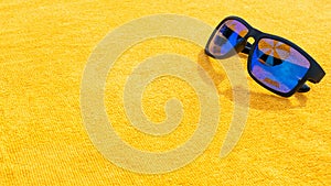 Black sunglasses summer background. Beach pool equipment with travel sunglasses on yellow holiday towel. Sun glasses