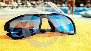 Black sunglasses summer background. Beach pool equipment with travel sunglasses on yellow holiday towel. Sun glasses