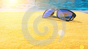 Black sunglasses summer background. Beach pool equipment with travel sunglasses on yellow holiday towel. Sun glasses