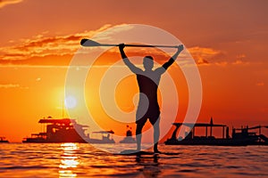 Black sunset silhouette of paddle boarder standing on SUP