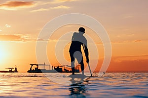 Black sunset silhouette of paddle boarder standing on SUP
