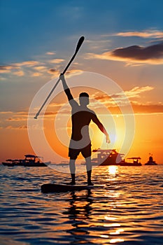 Black sunset silhouette of paddle boarder standing on SUP